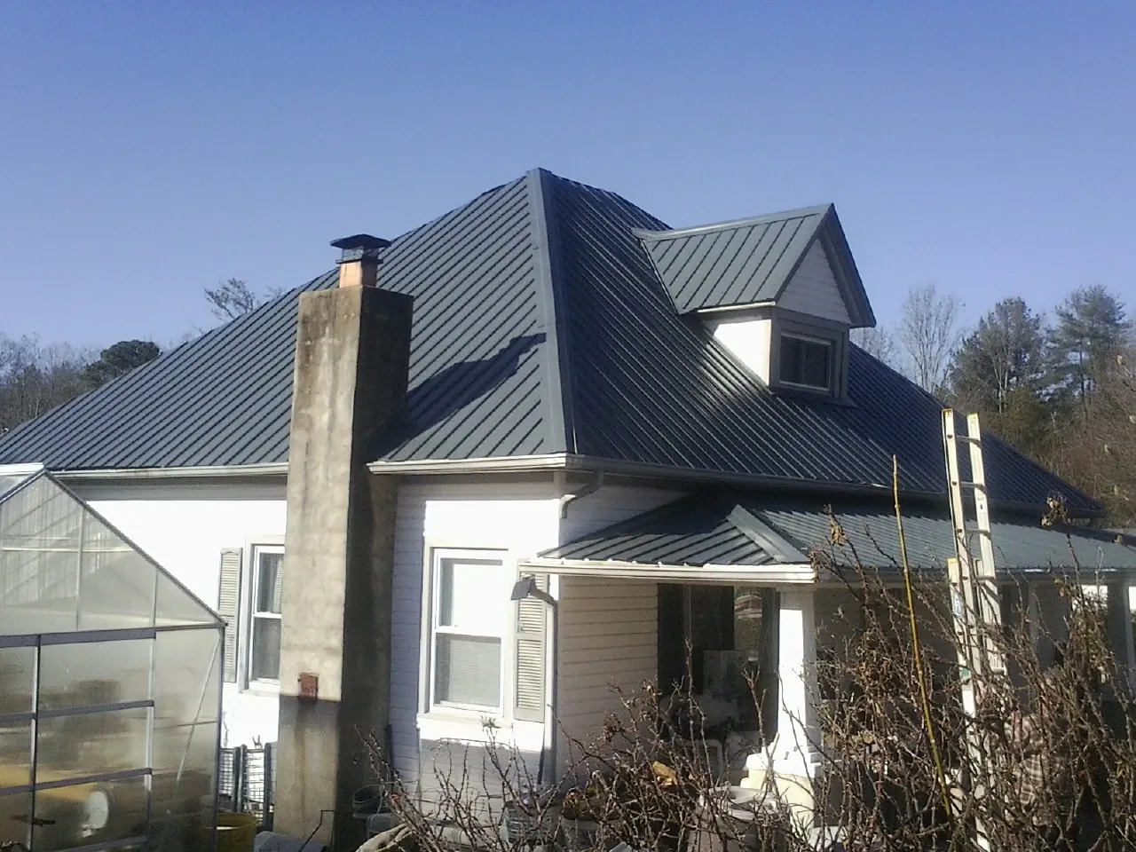 Dark blue standing seam metal roof on a white farmhouse with dormer — Slate & Tile Roof Repair by Roofing Brothers in Federalsburg