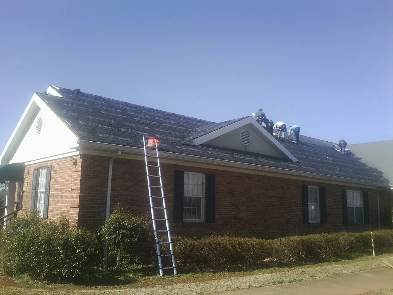 Crew tearing shingles off a brick ranch roof with a ladder set — Emergency Roof Repair work by our crew in Federalsburg