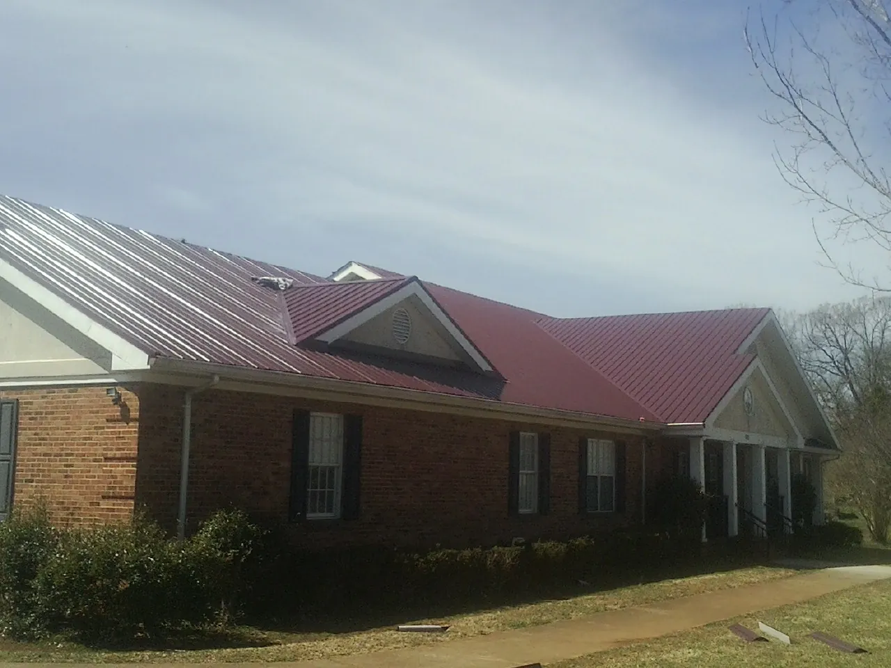 Red metal roof with gabled entries on a long brick building, from a Hail Damage Roof Repair job in Federalsburg