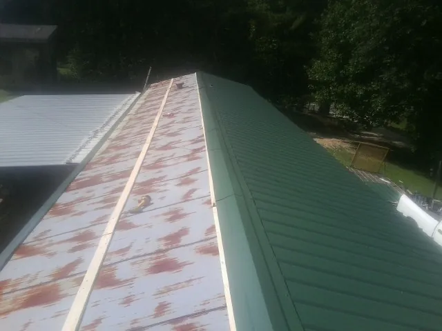 Old rusted panels beside newly installed green metal roofing — Wind Damage Roof Repair by Roofing Brothers in Federalsburg