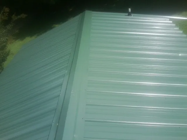 New green metal panels meeting at the ridge of a roof — Flat Roof Repair work by our crew in Federalsburg