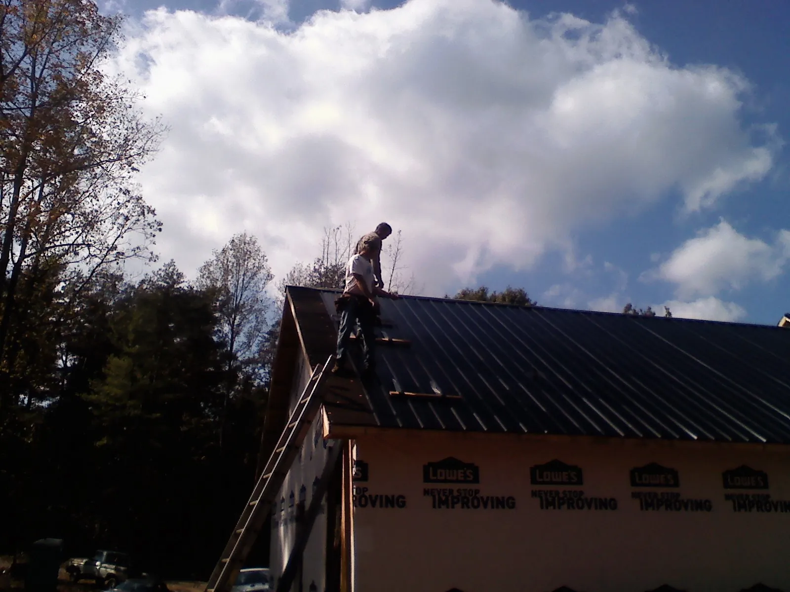 Roofer fastening dark metal panels high against a cloudy sky, from a Roof Inspection job in Federalsburg