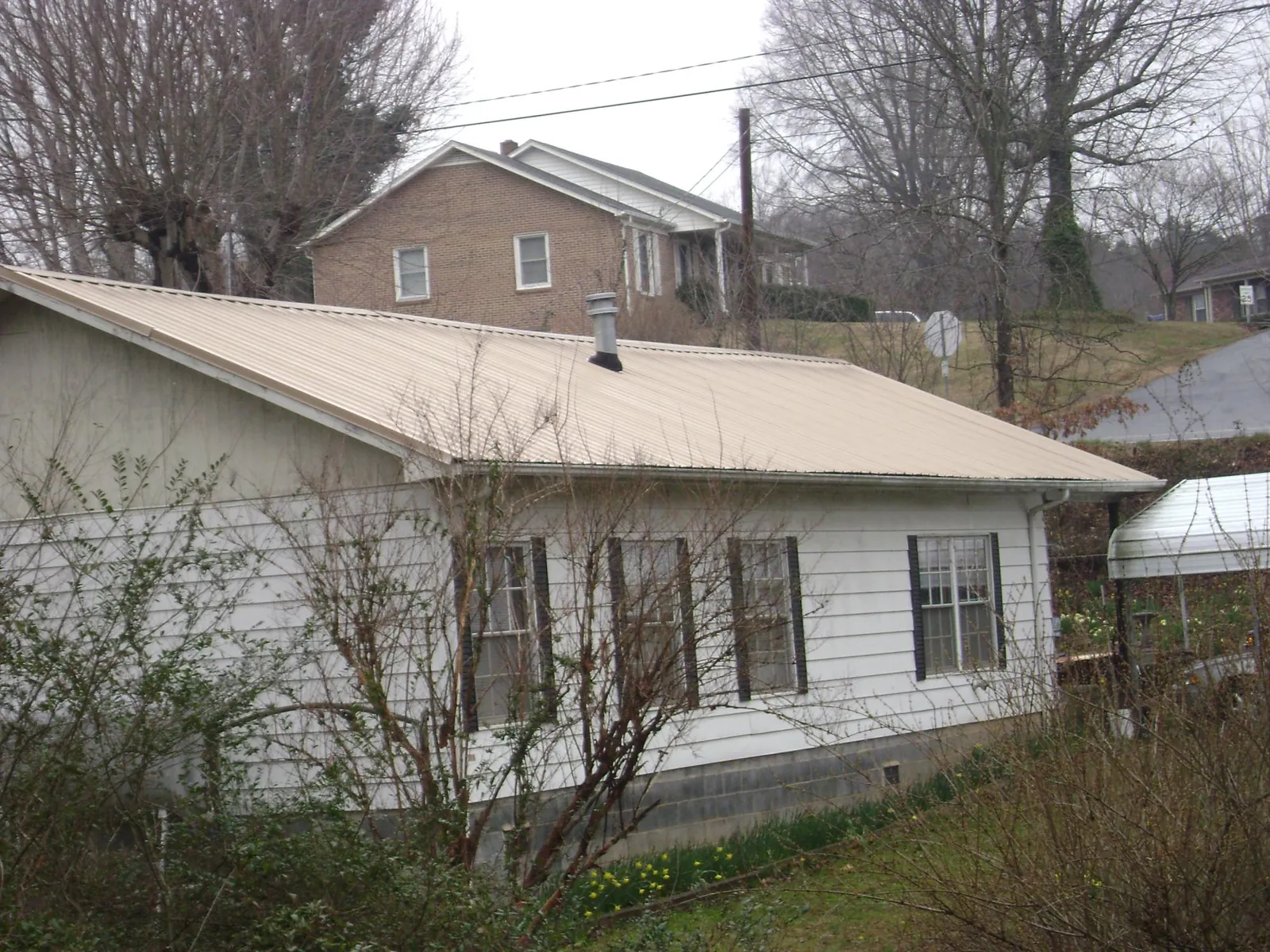 Tan metal roof on a white sided house set into a hillside — Commercial Roofing by Roofing Brothers in Federalsburg
